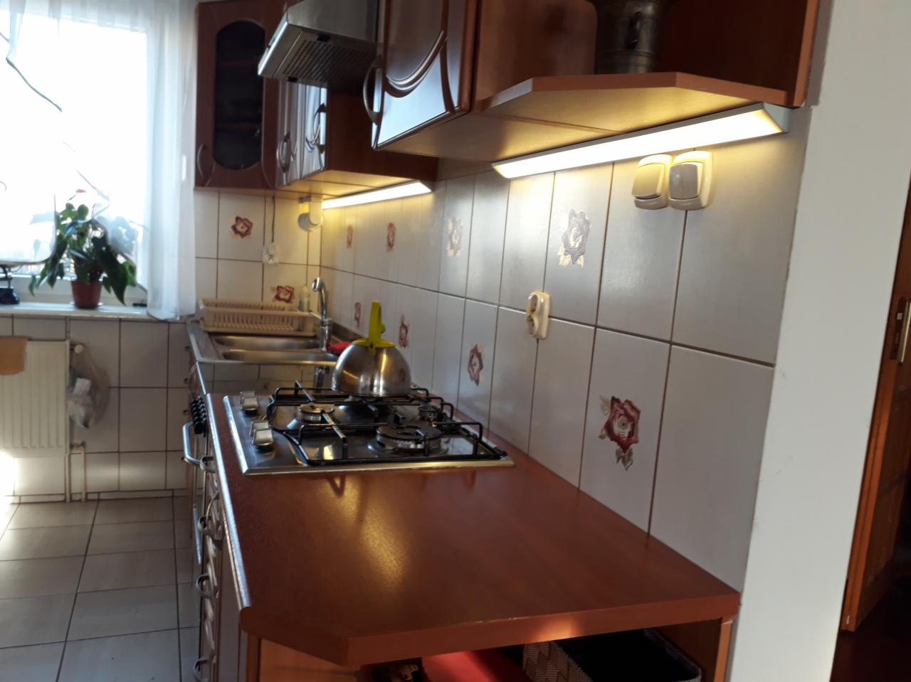 Kuchnia po remoncie z podświetleniem LED pod szafkami, widoczne gniazdka i wyłączniki na ozdobnych kafelkach.