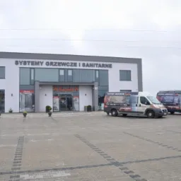 Budynek firmy z napisem 'Systemy grzewcze i sanitarne' oraz dwa samochody dostawcze z logo firmy 'Systemy Grzewcze Karles' na parkingu z kostki brukowej.