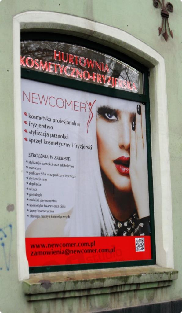 Plakat w oknie salonu kosmetycznego 'Hurtownia Kosmetyczno-Fryzjerska' z ofertą: kosmetyka profesjonalna, fryzjerstwo, stylizacja paznokci, sprzęt kosmetyczny i fryzjerski oraz szkolenia w zakresie...