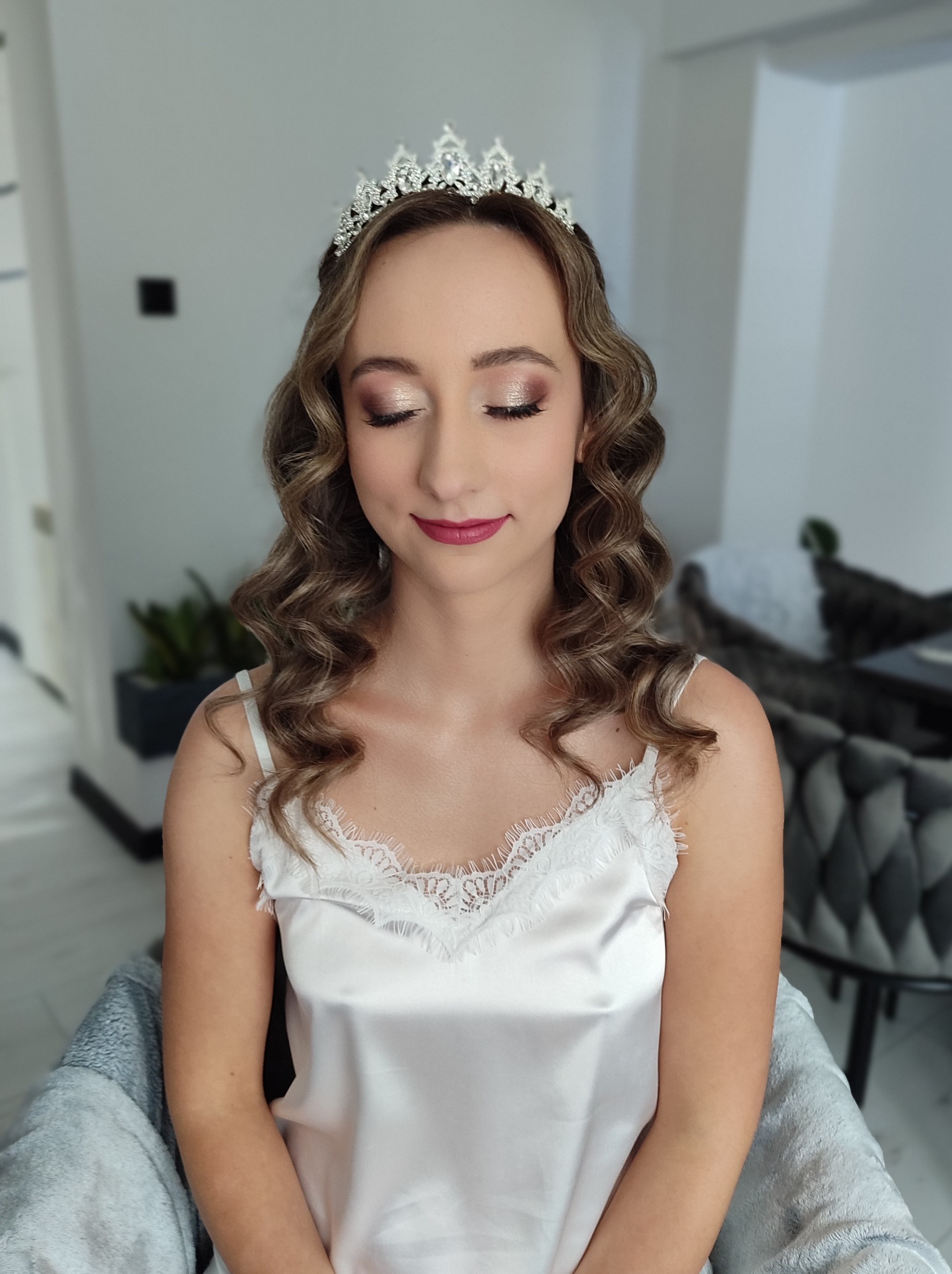 Panna młoda z zamkniętymi oczami, w tiarze, z delikatnym makijażem i upiętymi, kręconymi włosami w odcieniach blondu. Subtelna elegancja.