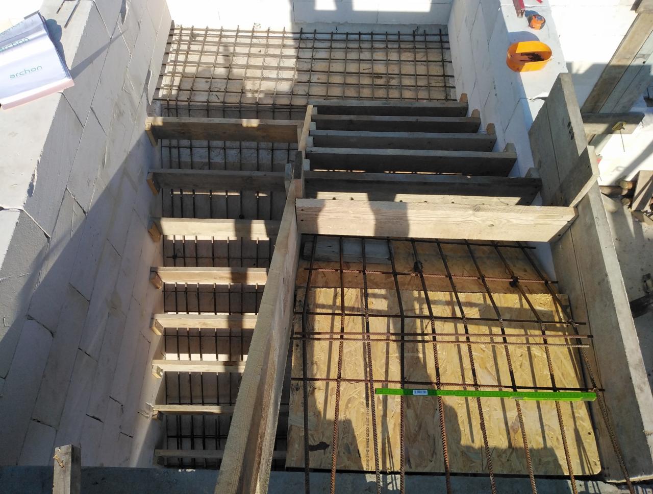 Budowa schodów z betonu komórkowego i zbrojenia stalowego, widoczne szalunki drewniane i narzędzia na górze.
