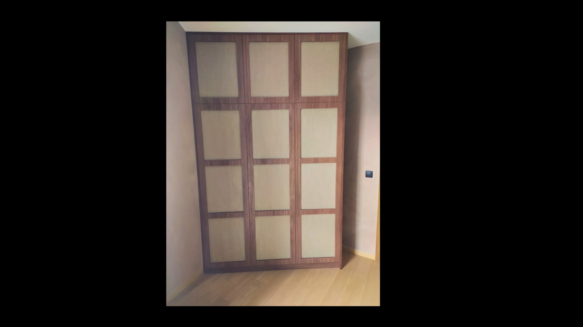 Drewniana szafa wnękowa z beżowymi frontami, podzielona na 12 segmentów, ustawiona na drewnianej podłodze w rogu pokoju o jasnych ścianach.