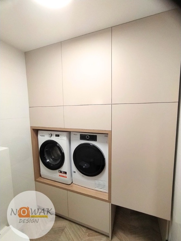 Jasna zabudowa meblowa w łazience z pralką i suszarką. Minimalistyczny design, gładkie fronty, drewniane akcenty. Funkcjonalna przestrzeń.