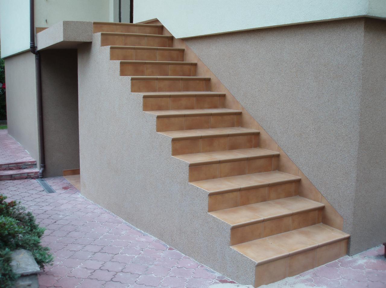 Zewnętrzne schody z terakoty prowadzące do budynku, z widoczną fakturą elewacji i brukowanym chodnikiem