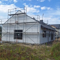 F.H.U MIESZBUD Grzegorz Mieszalski - Dom w trakcie tynkowania elewacji, otoczony rusztowaniem. Widoczne fragmenty elewacji z szarym tynkiem. Niebo z chmurami w tle.