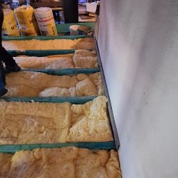 F.H.U MIESZBUD Grzegorz Mieszalski - Ocieplenie poddasza wełną mineralną, widoczne drewniane legary i worki z materiałem izolacyjnym. Prace izolacyjne w trakcie realizacji na strychu.