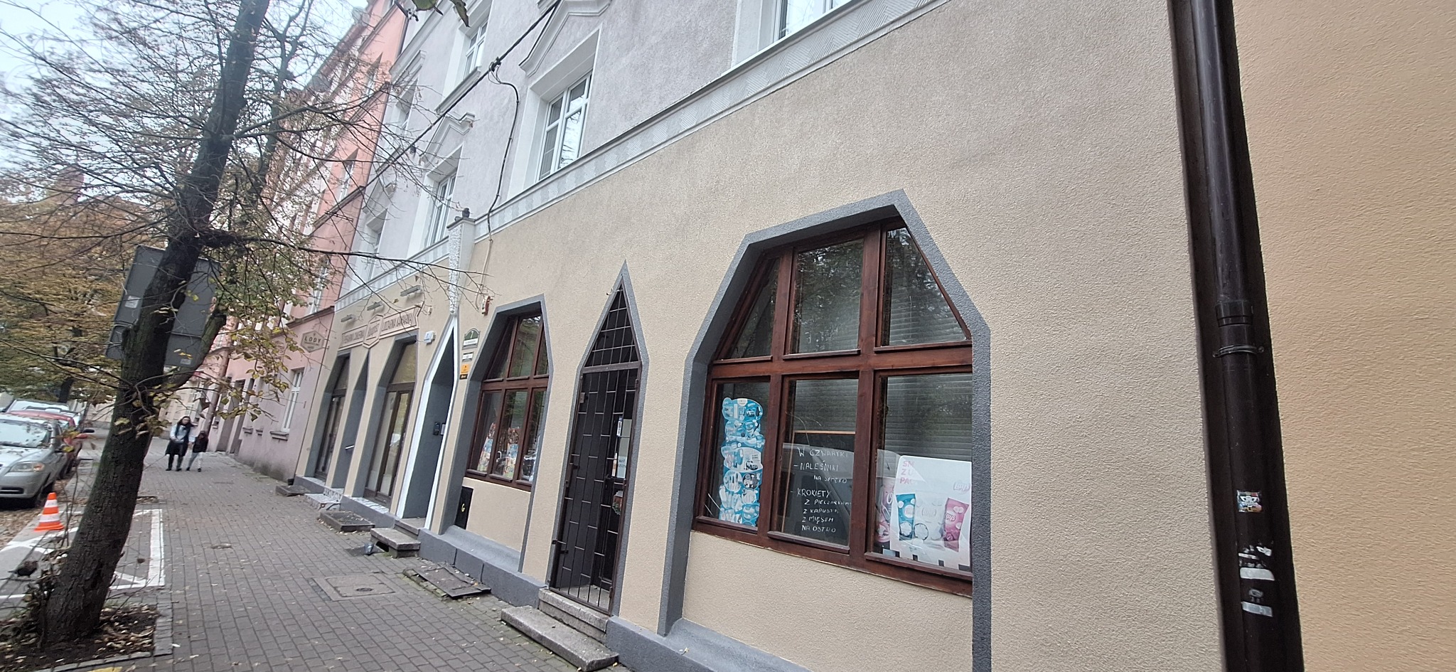 Elewacja kamienicy z oknami w kształcie łuku, widok z chodnika. Na elewacji widoczna rynna spustowa. Uwagę zwracają nietypowe okna i kolorystyka budynku.