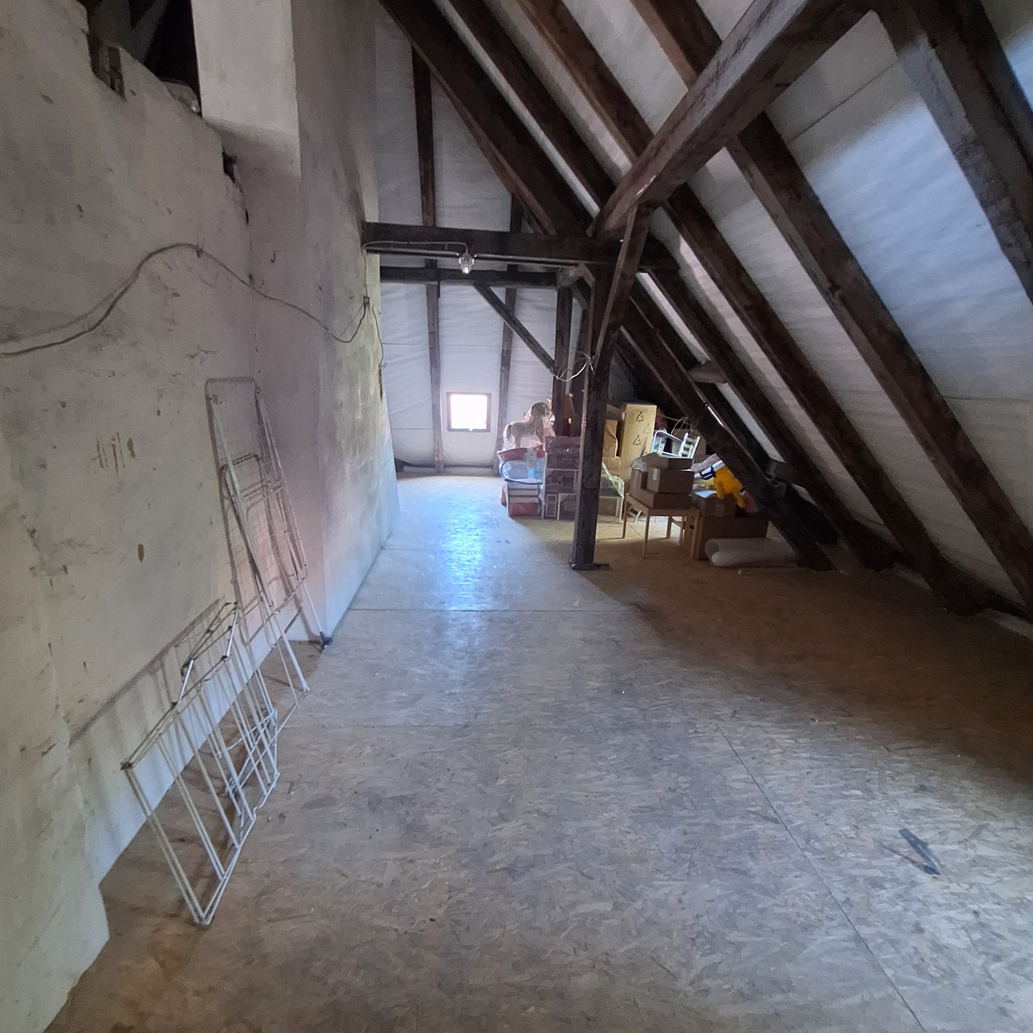 Poddasze z drewnianą konstrukcją dachu, ścianami w trakcie prac wykończeniowych i przygotowanym podłożem. Widoczne materiały i narzędzia.