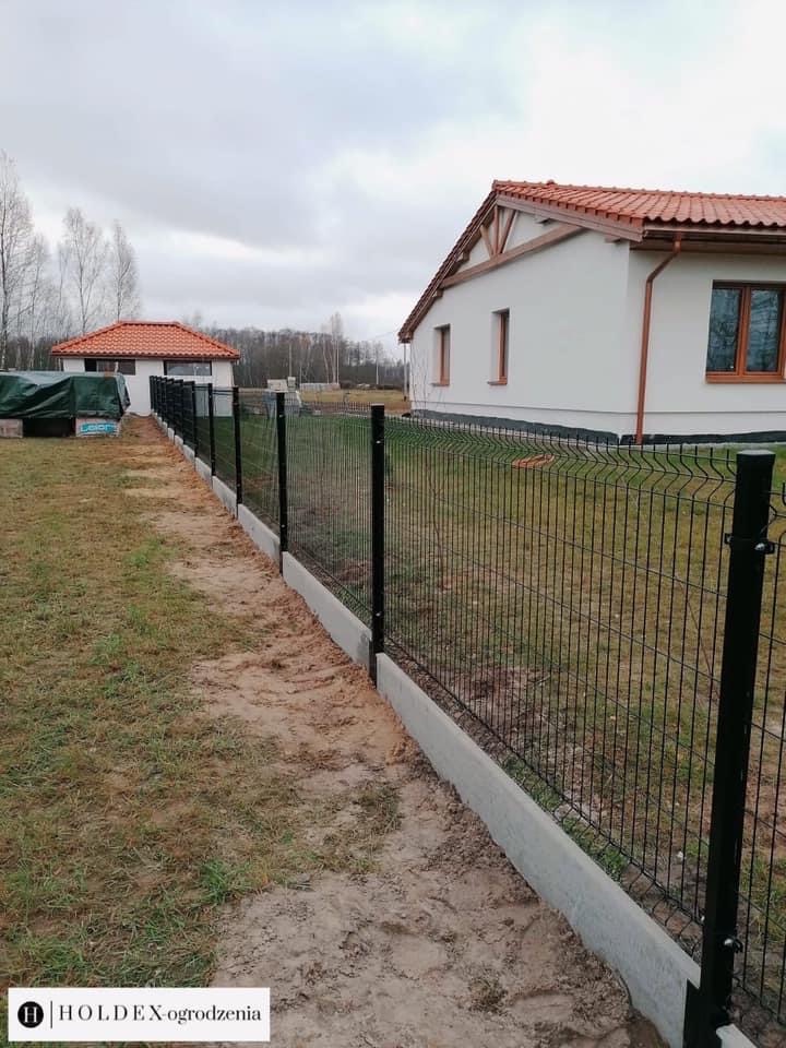 Nowoczesne ogrodzenie panelowe z podmurówką betonową, widok z boku, w tle budynek mieszkalny z czerwoną dachówką i trawnik.