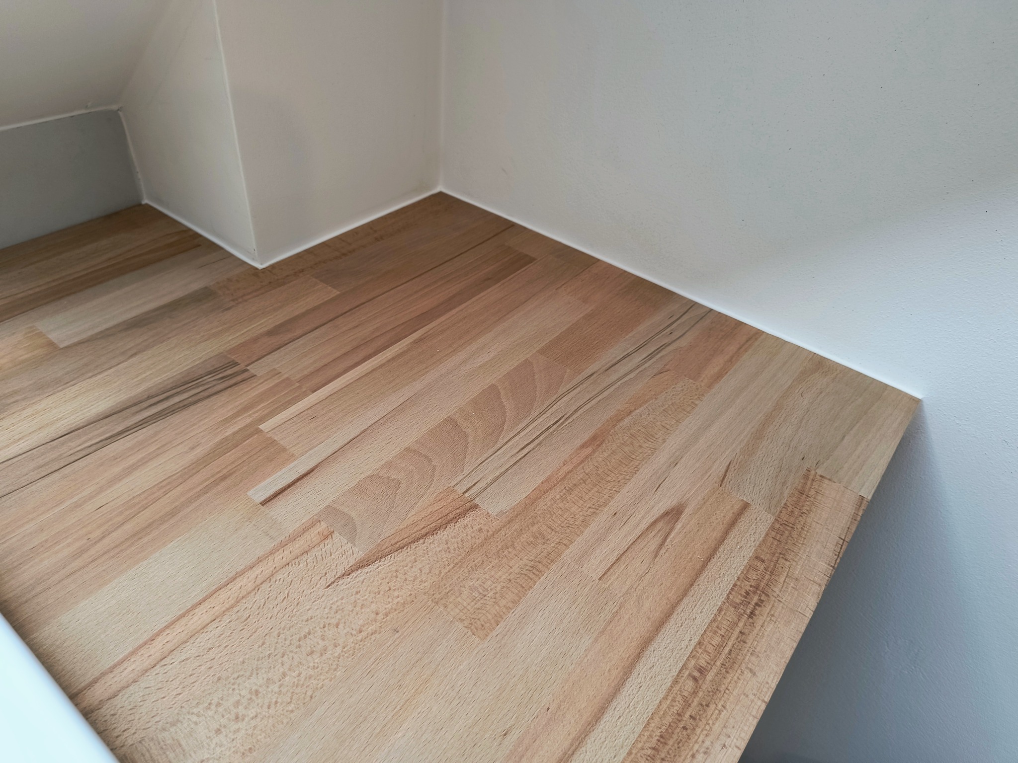 Blat drewniany z klejonego drewna bukowego, zamontowany w rogu pomieszczenia z białymi ścianami, widoczne detale struktury drewna i łączenia klejonego.