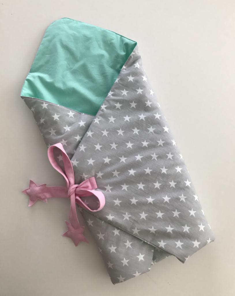 Dziecięcy otulacz w gwiazdki, związany różową wstążką z ozdobnymi gwiazdkami, widoczna miętowa podszewka.