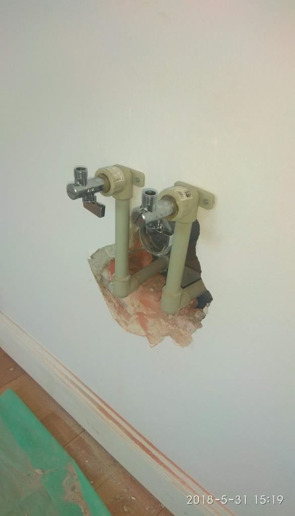 Dwa zawory grzejnikowe z rurami z tworzywa sztucznego wystające ze ściany, widoczne ślady po kuciu w tynku.