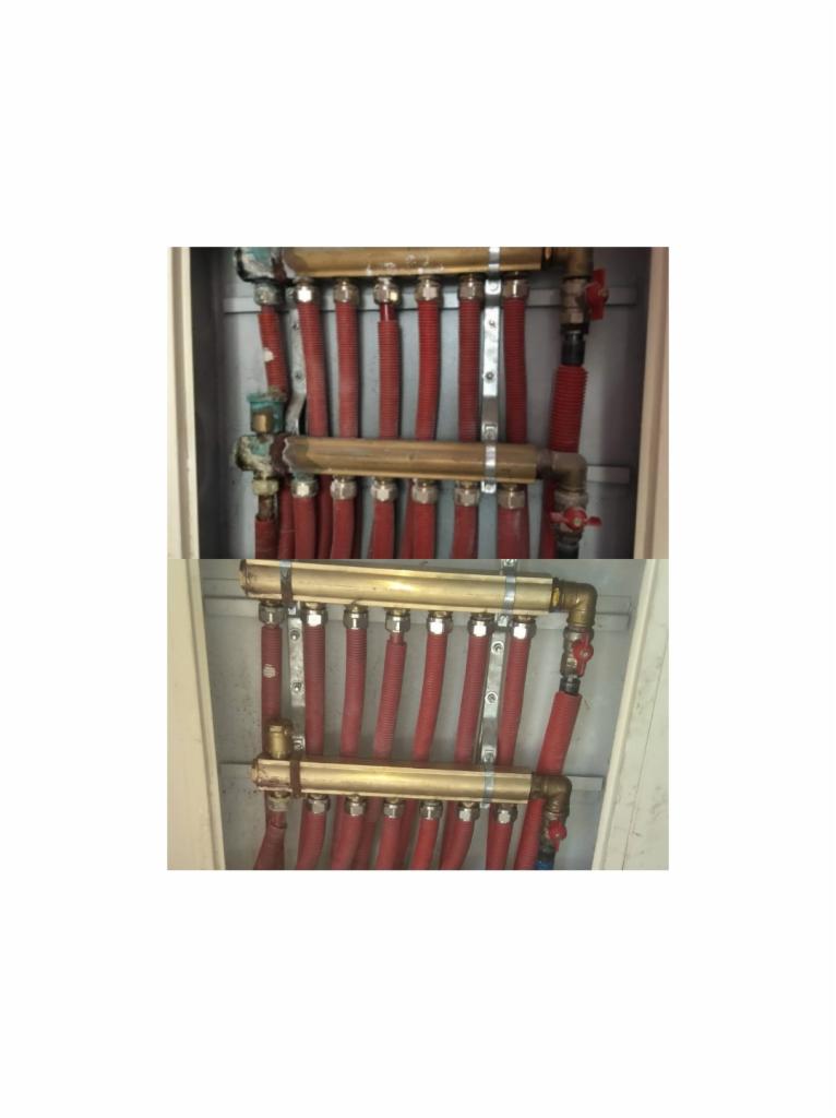 Rozdzielacz ogrzewania podłogowego z czerwonymi rurami w szafce, widoczne mosiężne elementy i zawory.