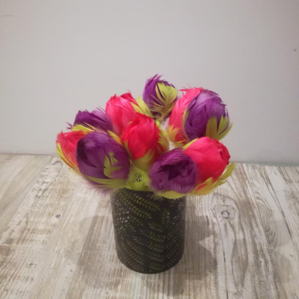 Dekoracyjny bukiet z piór w odcieniach różu, fioletu i limonki, umieszczony w czarnym, ażurowym wazonie z motywem liści na drewnopodobnym blacie.