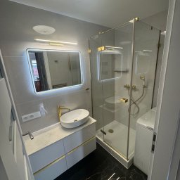 Grupa prace wykończeniowe - Nowoczesna łazienka z kabiną prysznicową, umywalką na szafce i lustrem z podświetleniem LED. Czarne marmurowe płytki podłogowe. Złote akcenty.