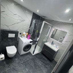 Grupa prace wykończeniowe - Nowoczesna łazienka z marmurowymi płytkami, kabiną prysznicową, umywalką z szafką i pralką. Minimalistyczny design z oświetleniem LED.