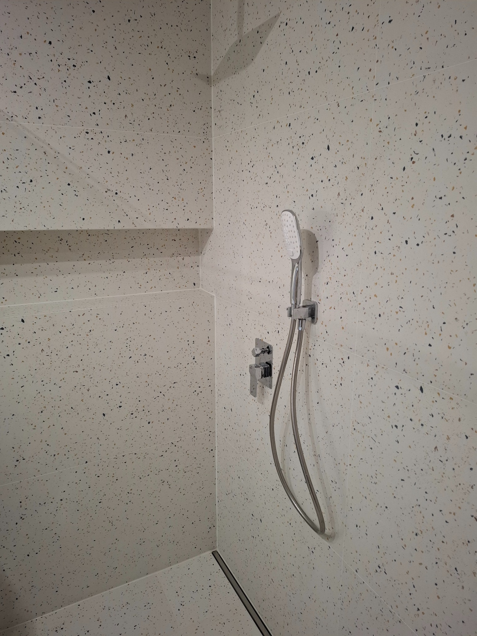 Nowoczesna kabina prysznicowa wykończona płytkami imitującymi lastryko, z zamontowaną baterią i słuchawką prysznicową.