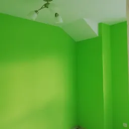 Świeżo pomalowane na jaskrawy zielony kolor ściany w pokoju, widoczny fragment sufitu z lampą z trzema kloszami i fragment ściany w stanie surowym.
