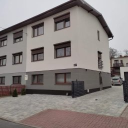 Mar-Bud - Dwukondygnacyjny dom z elewacją w dwóch odcieniach szarości i brązowymi roletami, numer domu 27, widok z poziomu ulicy w pochmurny dzień.