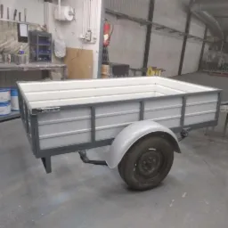 Nowa, pomalowana na szaro przyczepka samochodowa z białym wnętrzem skrzyni, stojąca w hali produkcyjnej.