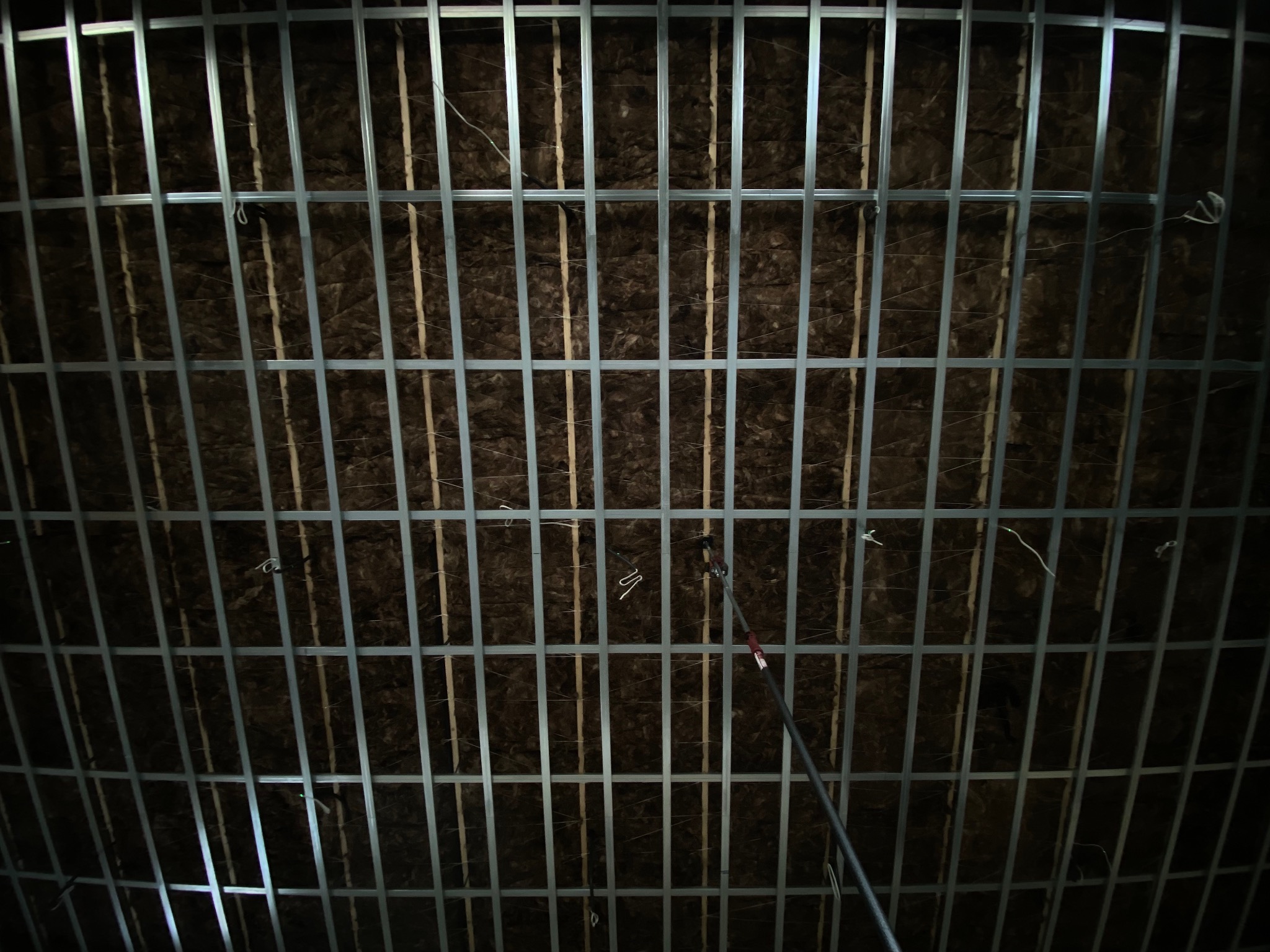 Sufit z izolacją z wełny mineralnej i metalowym rusztem, widok z dołu. Widoczne przewody i elementy mocujące. Oświetlenie punktowe.