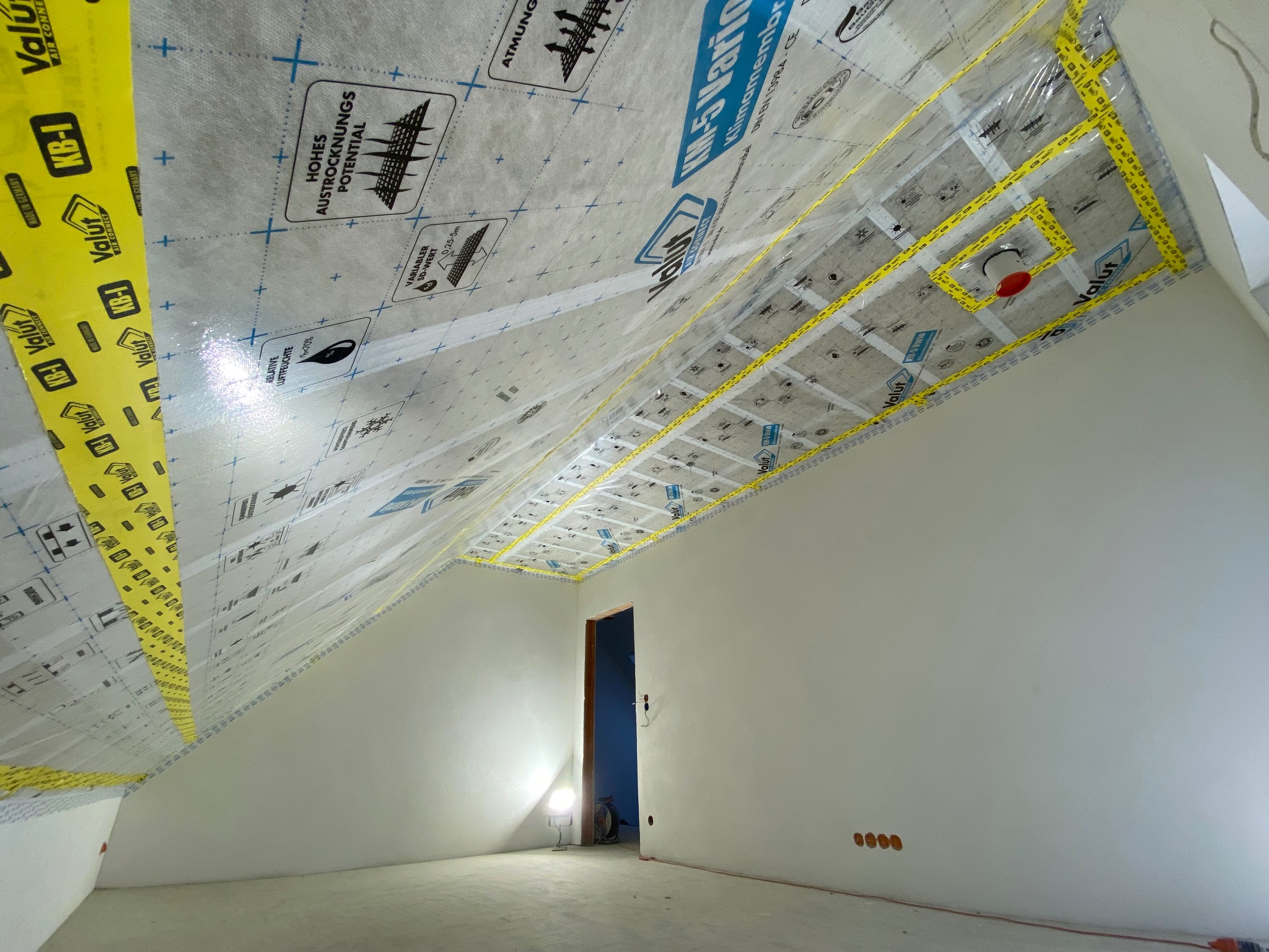 Poddasze w trakcie ocieplania: folia paroizolacyjna z taśmami Valut KB-1, widoczne elementy instalacji. Praca w toku, surowe ściany, przygotowanie do dalszych prac wykończeniowych.