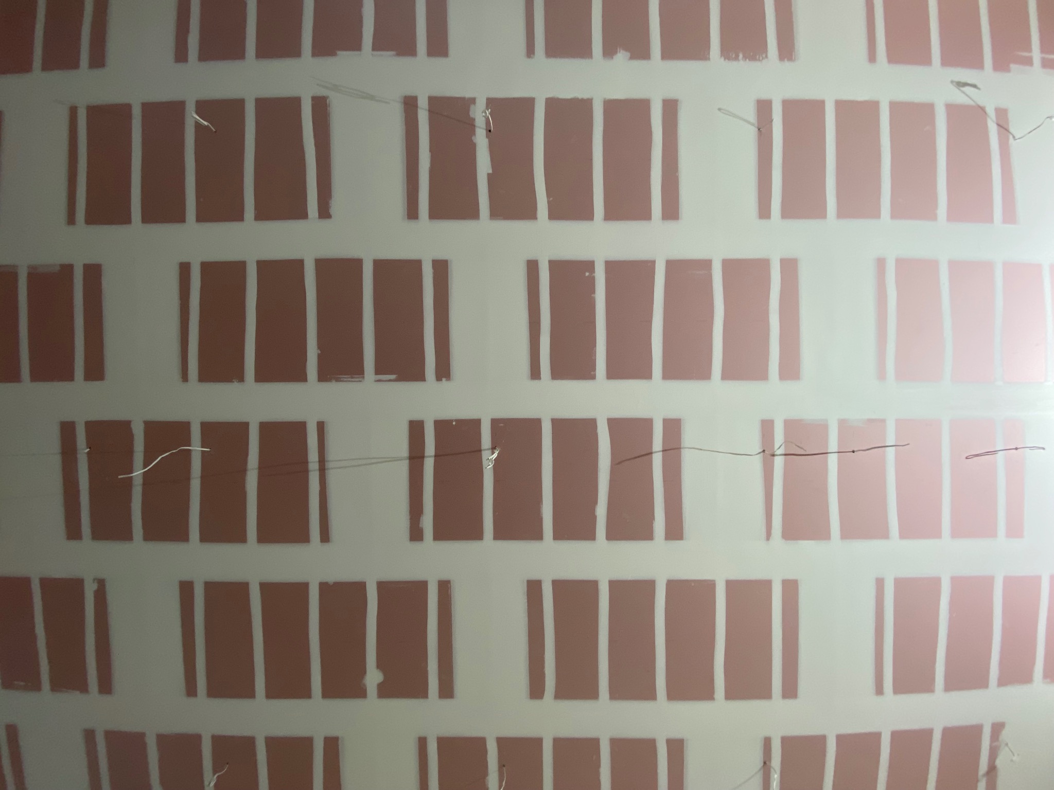 Ściana po nałożeniu farby podkładowej z widocznymi pasami, przygotowana do malowania dekoracyjnego. Widoczne drobne niedoskonałości i nitki.