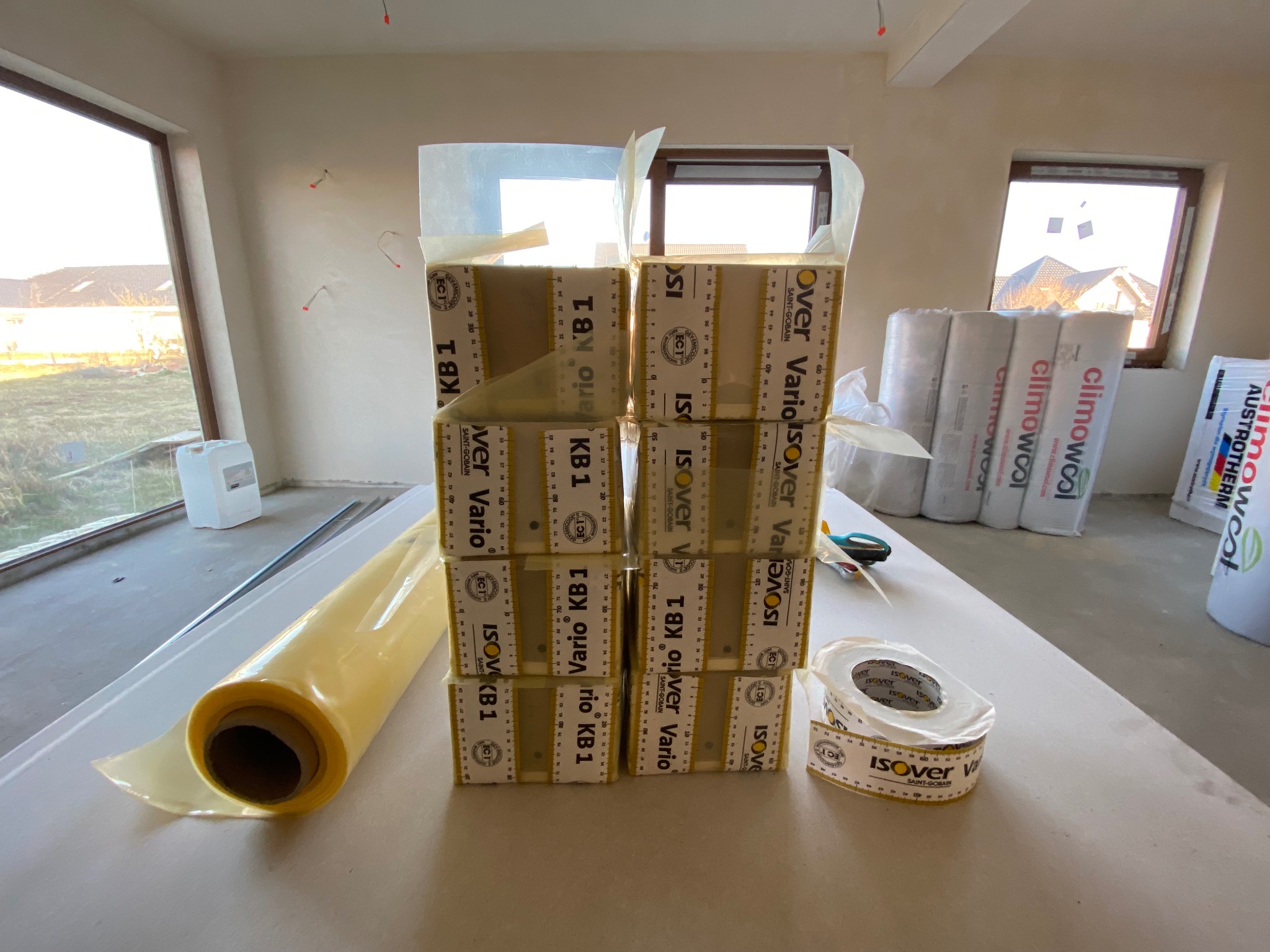 Materiały izolacyjne Isover Vario KB 1, folia i taśma uszczelniająca na tle wnętrza w trakcie ocieplania. Widoczne rolki wełny Climowool. Przygotowanie do ocieplenia poddasza.