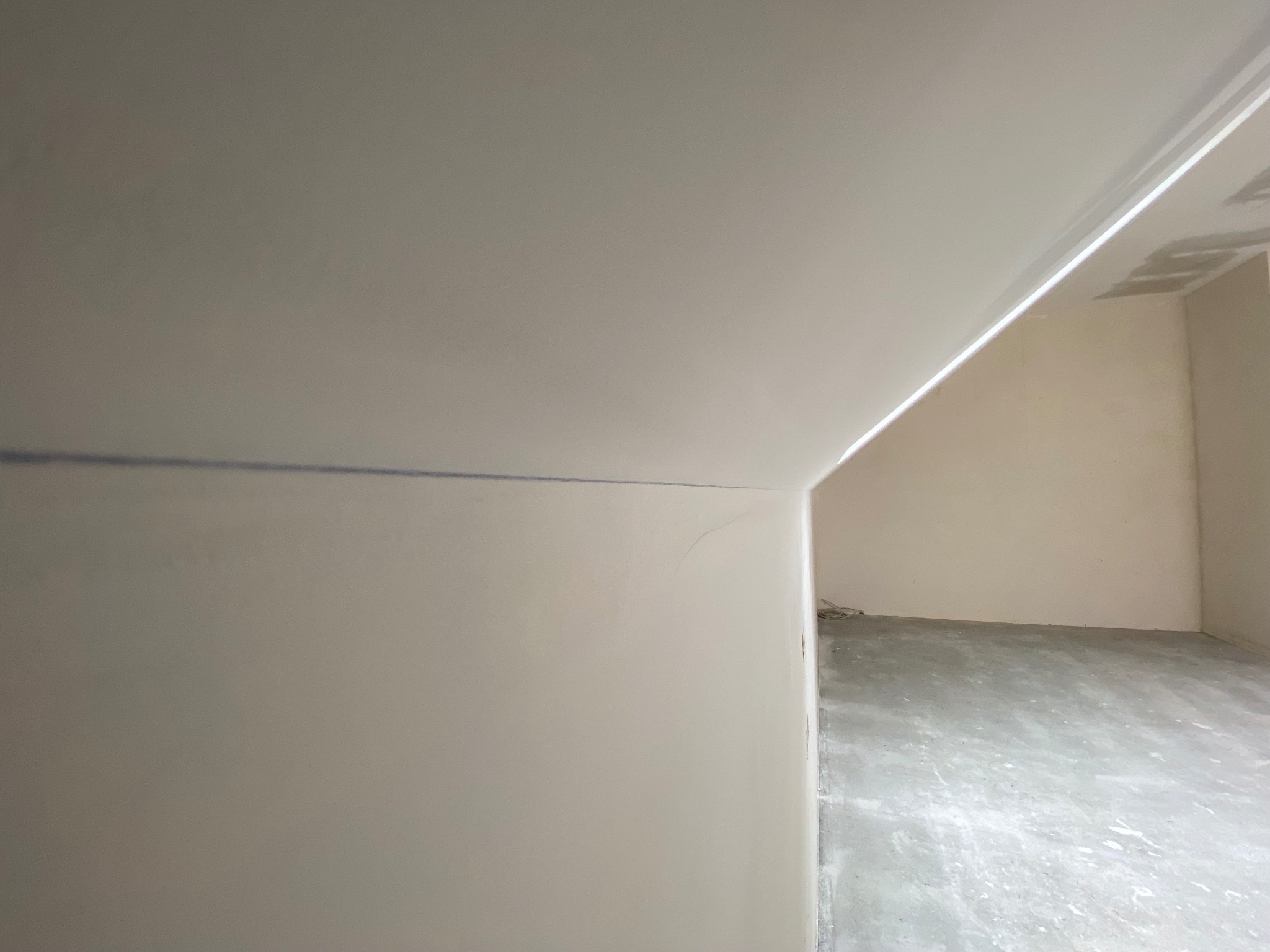 Wnętrze po montażu płyt kartonowo-gipsowych: gładkie ściany i sufit, widoczne łączenia gotowe do szpachlowania. Szare podłoże, przygotowanie do dalszych prac wykończeniowych.