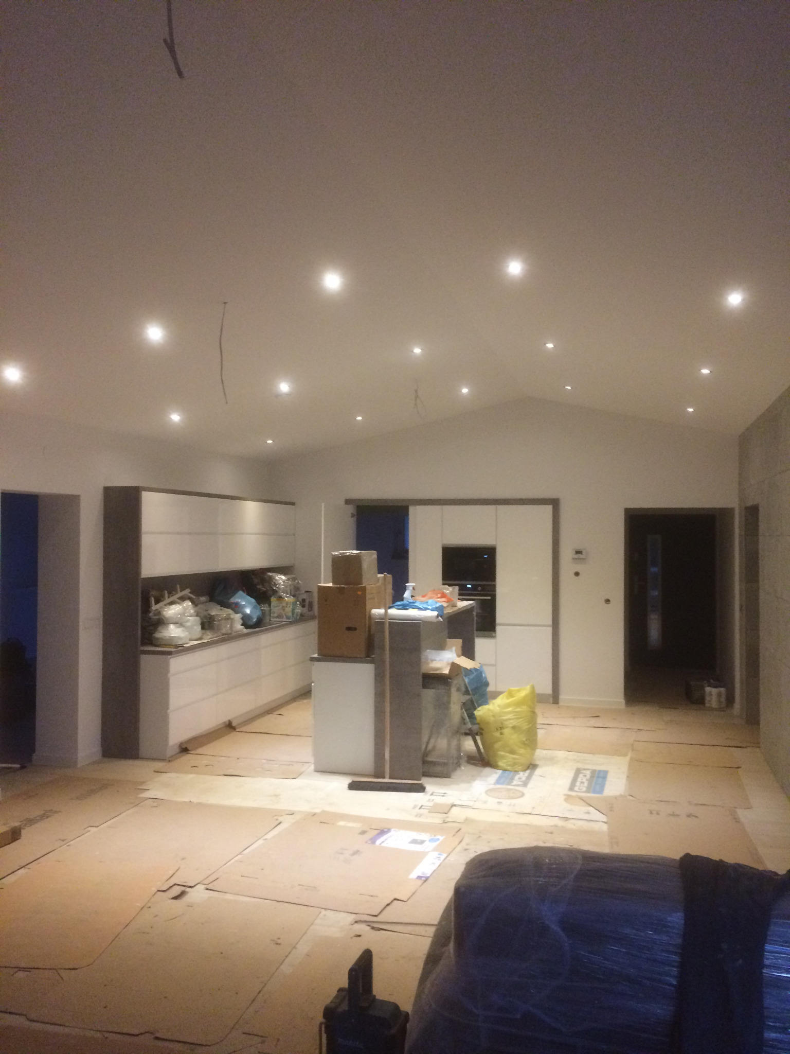 Wnętrze domu w trakcie prac wykończeniowych: położone kartony ochronne na podłodze, zabudowa kuchenna w trakcie montażu, widoczne narzędzia i materiały budowlane.