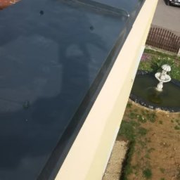 Express Team - Widok z góry na fragment dachu z nowym, błyszczącym, ciemnoszarym obrzeżem, widoczna część starego, czerwonego dachu, ściana budynku w kolorze kremowym, w tle fontanna i samochód.