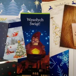 Stos kartek okolicznościowych z życzeniami świątecznymi, o różnej stylistyce i grafice, ułożonych na płasko, w tym kartka z motywem śląskim i kopalnią w tle.