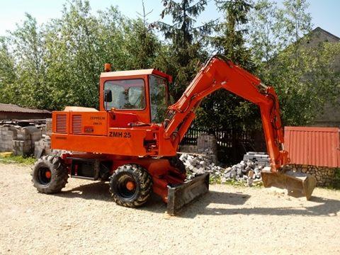 Pomarańczowa koparka kołowa Zeppelin ZMH 25 na żwirowym podłożu, z stertą gruzu i kostki w tle, gotowa do pracy.