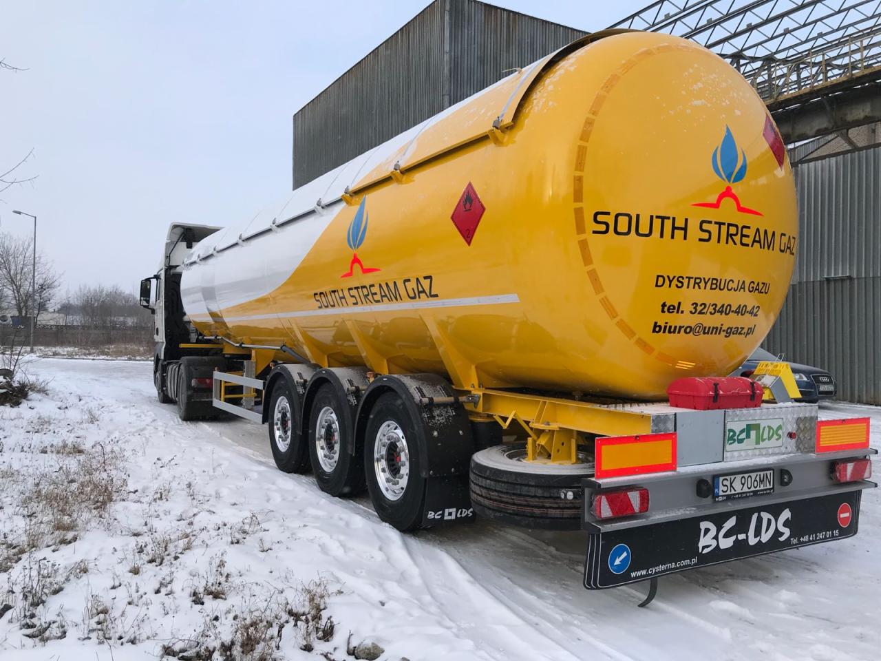 Żółto-biała cysterna z logiem South Stream Gaz na śniegu. Widoczny fragment budynku w tle. Numer rejestracyjny SK 906MN.