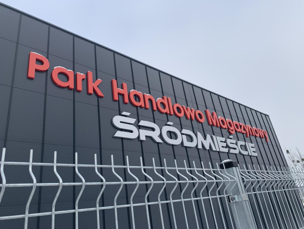 Budynek Parku Handlowo Magazynowego Śródmieście z widoczną metalową siatką ogrodzeniową na pierwszym planie.