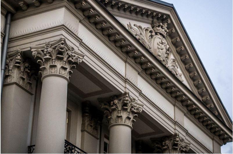 Fasada budynku z kolumnami korynckimi, dekoracyjnym fryzem i zabezpieczeniem przed ptakami na gzymsie, widok z dołu