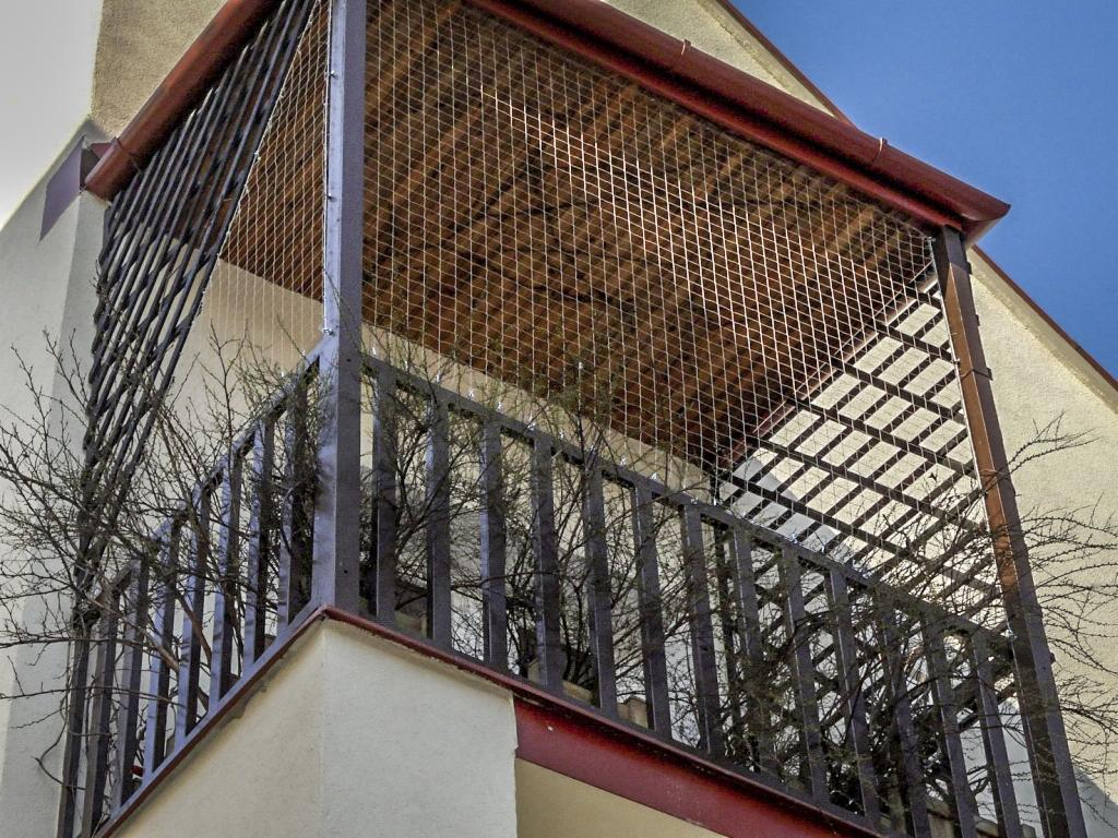 Zabezpieczony siatką balkon z metalową balustradą, widok z dołu na tle błękitnego nieba.