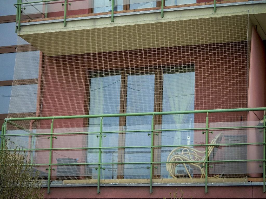 Zabezpieczenie balkonu siatką ochronną przed ptakami w Krakowie, widok z dołu na balkon z zieloną barierką i zwiniętym wężem ogrodowym wewnątrz.