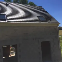 Szary dach z dachówki ceramicznej z dwoma oknami dachowymi na surowym budynku z betonu komórkowego w słoneczny dzień.