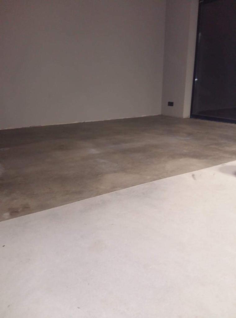 Przygotowanie podłoża pod wylewkę samopoziomującą w nowym pomieszczeniu, widoczna granica między surowym betonem a zagruntowaną powierzchnią.