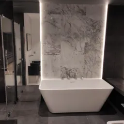 Nowoczesna, wolnostojąca wanna w minimalistycznej łazience z marmurową ścianą i podświetleniem LED.