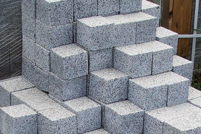 Szare kostki o porowatej strukturze, ułożone w stos, widoczne elementy drewniane w tle.