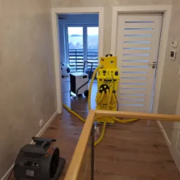 Profesjonalny sprzęt do osuszania w trakcie pracy w korytarzu z drewnianą podłogą, widoczny osuszacz kondensacyjny i wentylator osuszający.