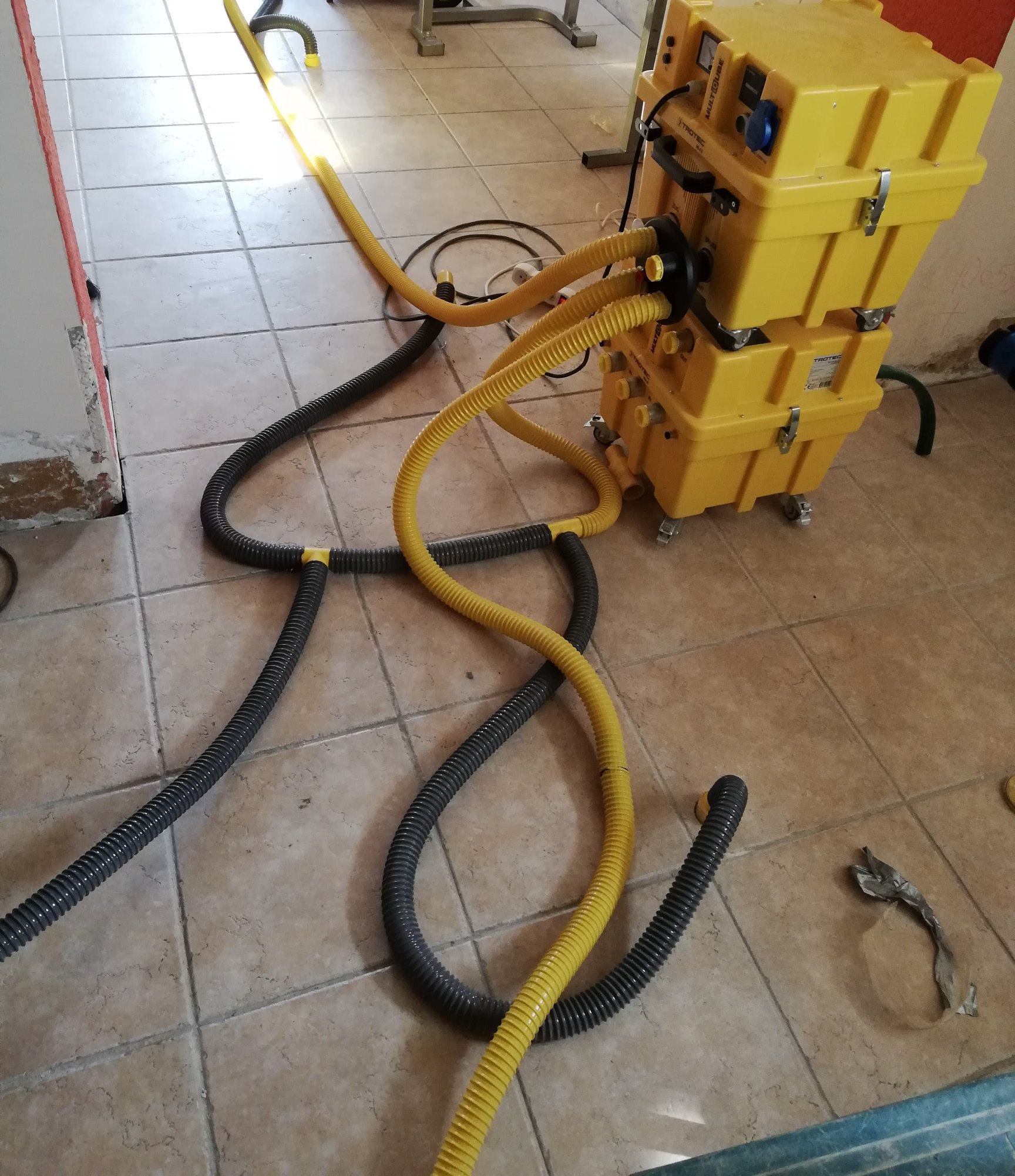 Żółty, dwuczęściowy agregat z kilkoma podłączonymi wężami w kolorach żółtym i czarnym, stojący na brązowych płytkach w pomieszczeniu w trakcie pracy.