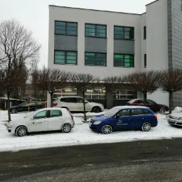 Zimowy widok na budynek warsztatu samochodowego z zaparkowanymi, lekko ośnieżonymi autami przed wejściem.