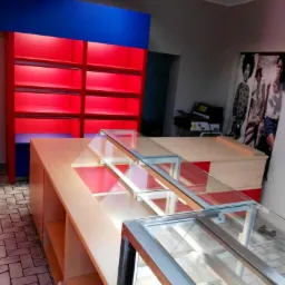 Nowoczesne, podświetlane regały i przeszklone lady sklepowe w kolorystyce czerwono-niebieskiej, ustawione w pomieszczeniu z płytkami podłogowymi i plakatem na ścianie.