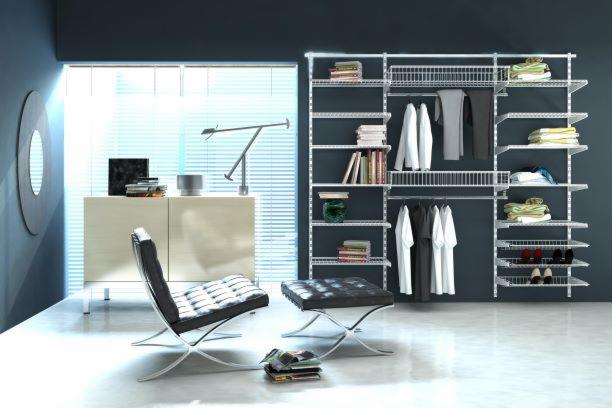 Nowoczesna garderoba z białym systemem regałów i półek, uzupełniona o skórzany fotel Barcelona i taboret, ustawione na tle okna z żaluzjami.