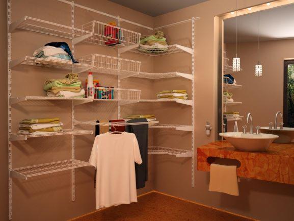 System półek i koszy drucianych, zamontowany w rogu pomieszczenia, z ułożonymi ręcznikami i ubraniami, widoczne również umywalki i lustro w tle.