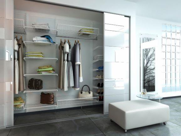 Wnętrze garderoby z przesuwnymi drzwiami, wyposażone w system półek, koszy i wieszaków na ubrania, torby i inne akcesoria, oświetlone jasnym światłem dziennym w nowoczesnym stylu.