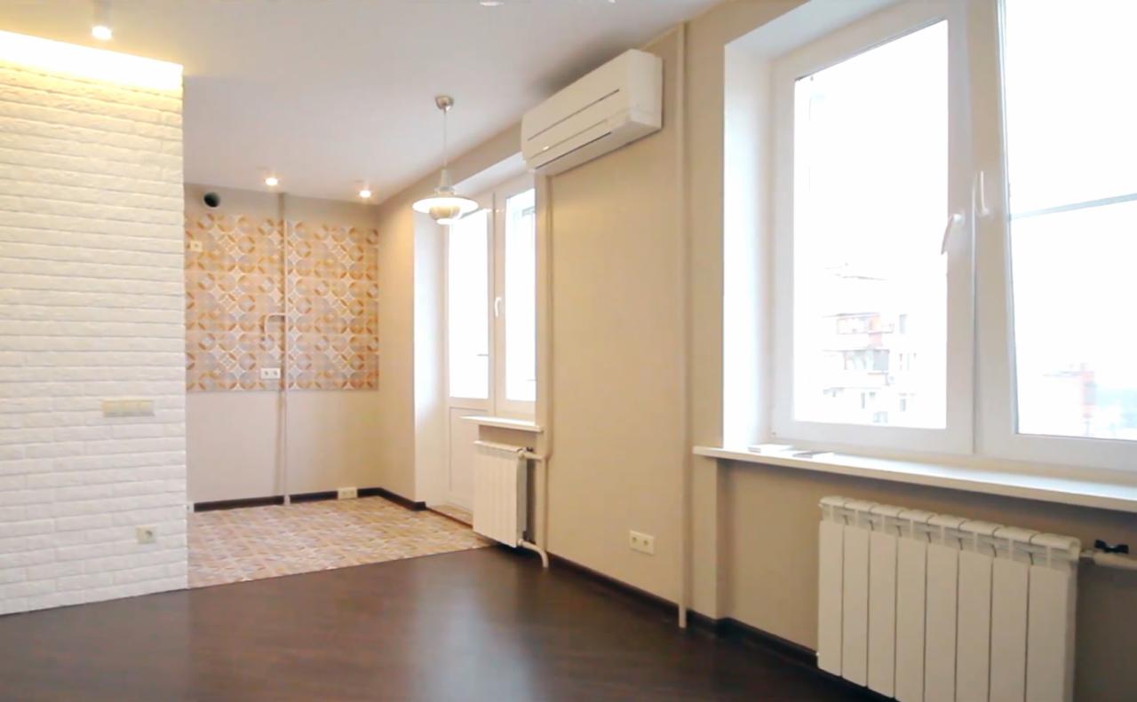 Jasne, puste pomieszczenie po remoncie z panelami podłogowymi w kolorze ciemnego drewna, białą ścianą z cegły dekoracyjnej, wzorzystą tapetą na ścianie w tle, białymi grzejnikami pod oknami...